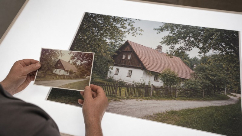 Muž u notebooku porovnává starou rozmazanou fotografii s její zvětšenou verzí v programu na upscaling